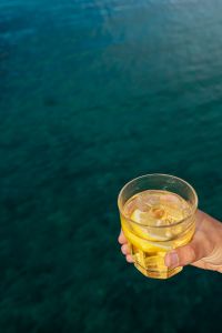 Kaboompics - Hand Holding a Yellow Drink over Dark Teal Seawater