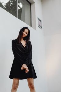 Kaboompics - Asian Woman in Black Satin Wrap Dress with Hands Clasped against White Wall