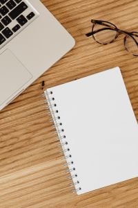 Kaboompics - White Laptop, Eyeglasses and Empty Spiral Notebook on a Wood Desk, Overhead Workspace Flat Lay