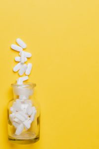 Kaboompics - White Tablets Falling from Yellow Bottle on Bright Yellow Background