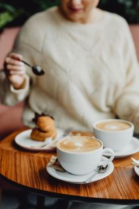 Kaboompics - Woman Holding a Spoon over a Pastry with Cappuccino on a Cafe Table