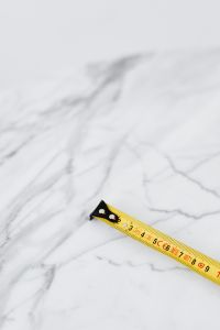 Kaboompics - Minimal Tape Measure Hook and Short Yellow Blade against Veined Marble, Vertical Tool Photo