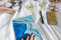 Kaboompics - Woman Holding Blue Patterned Planner beside Gold Smartphone on White Bedding