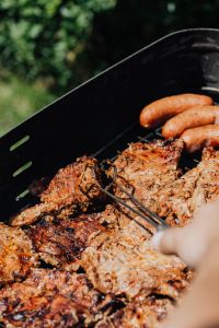 Kaboompics - Outdoor Charcoal Grill Loaded with Pork Neck Steaks and Sausages, Hand Turning Meat