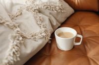 Kaboompics - Cream Coffee in a White Cup Beside a Fringed Throw on Cognac Leather, Cozy Home Styling