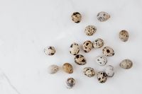 Kaboompics - Speckled Quail Eggs Scattered on White Marble with Wide Copy Space, Easter Flat Lay