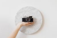 Kaboompics - Minimal Film Camera on a Round Marble Surface with a Supporting Hand