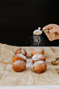 Kaboompics - Gold Spoon Sprinkling Powdered Sugar over Polish Paczki against a Dark Backdrop