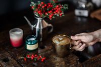 Kaboompics - Close-Up of a Latte Held by Hand beside Red Holly Berries and a Candle