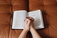 Kaboompics - Hands in Prayer over an Open Bible on a Leather Sofa