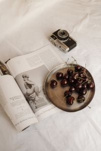 Kaboompics - Open Book, Cherries and Vintage Camera on White Bedding