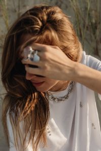 Kaboompics - Woman Covering Sunglasses with Ringed Hand, Chain Necklace and White Shirt, Beach Fashion Portrait
