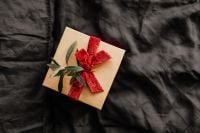 Kaboompics - Kraft Paper Christmas Gift with a Red Ribbon on Dark Bedding