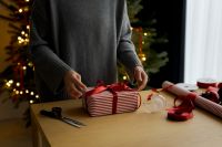 Kaboompics - Person Wrapping Red Ribbon Gift beside Christmas Tree