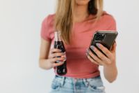 Kaboompics - Woman Holding a Smartphone and Cola Bottle in a Pink Top, Casual Lifestyle and Social Media Content