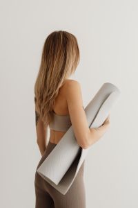 Kaboompics - Woman Holding a Rolled Yoga Mat Against a Light Wall