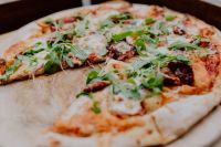 Kaboompics - Arugula Pizza on a Wooden Serving Board in a Cozy Restaurant