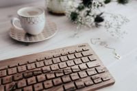 Kaboompics - Coffee Cup and Wooden Keyboard with Flowers and Gold Necklace