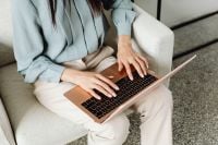 Kaboompics - Asian Woman Typing on a Laptop in a White Armchair