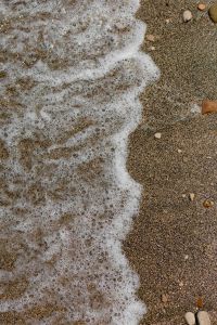 Kaboompics - Sea Foam Spreading across a Sandy Pebble Beach Close-Up