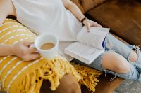 Kaboompics - Woman with a cup of coffee & book, yellow blanket, blue jeans pants