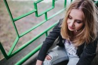 Kaboompics - Blonde woman in a black jacket and ripped jeans by a green handrail