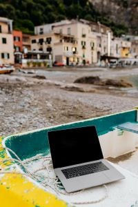 Kaboompics - Open MacBook on a Yellow Boat with Pebble Shore and Coastal Buildings