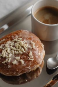 Kaboompics - Glazed Pastry with White Chocolate Shavings beside Coffee, Close-Up Breakfast Still Life