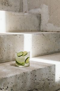 Kaboompics - Small Cucumber and Lime Water Glass Low in Frame on Sunlit Concrete Stairs, Tall Minimal Background with Copy Space