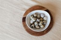 Kaboompics - White Bowl of Speckled Eggs on a Round Wooden Board, Minimalist Easter Table Styling