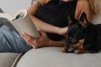 Kaboompics - Woman Reading on the Sofa beside Her Resting Small Dog