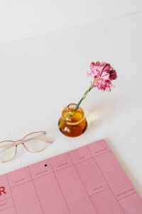 Kaboompics - Pink Calendar and Glasses with Carnation in Amber Glass Vase for Minimal Desk Styling