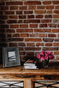 Photo frame, books and pink flowers in a vase on a wooden commode