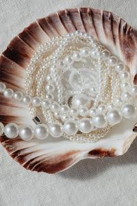 Kaboompics - White Pearl Necklace Coiled Inside a Scallop Shell on Beige Linen, Overhead Still Life