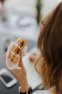 Kaboompics - Woman Eating Sandwich Beside Notebook at Office Desk