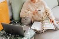 Kaboompics - The woman is drinking tea on the couch, reading the newspaper and using a laptop
