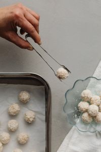 Kaboompics - Hand Arranging Coconut Truffles with Metal Tongs on a Bright Kitchen Counter, Homemade Candy Prep