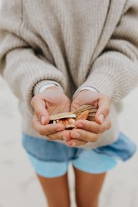 Kaboompics - Young Woman Holding Seashells on a Sandy Beach, Knit Sweater and Denim Shorts Summer Vacation