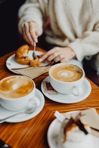 Kaboompics - Coffee and Pastry on a Wooden Cafe Table with the Diner in Frame