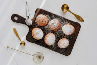 Kaboompics - Polish Doughnuts on Dark Board with Brass Sifter and Spoons