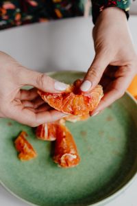 Kaboompics - A woman peels an orange on a green plate