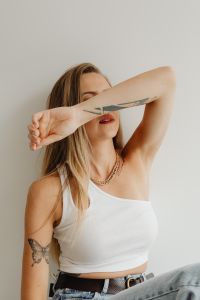 Kaboompics - Portrait of Woman Shielding Her Face with Tattooed Arm, White Top and Casual Denim