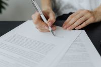 Kaboompics - Hand Completing Contract Paperwork Beside Smartphone in Office