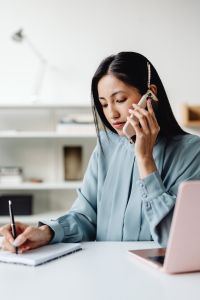 Kaboompics - Focused Asian Woman Taking a Phone Call While Writing at Her Desk