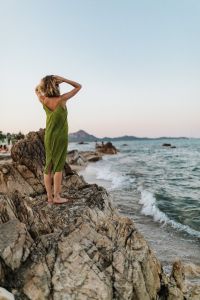 Kaboompics - Woman in a Green Summer Dress Touching Her Hair on the Shore, Breezy Coastal Travel Photo