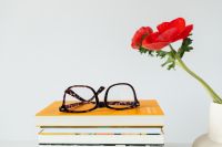 Kaboompics - Tortoiseshell Glasses on a Yellow Book with Red Poppy Vase