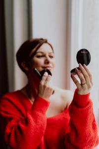 Kaboompics - A woman in a red sweater does her make-up - applies a foundation with a brush