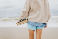 Kaboompics - Back View of a Woman Carrying Books Along the Shore in a Knit Sweater and Denim Shorts