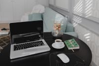 Kaboompics - Sunlit Home Office Table with Open Laptop, Coffee, Wireless Mouse and Botanical Notebook