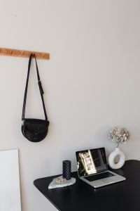Kaboompics - Wall-Mounted Black Shoulder Bag above Laptop Desk with Candle and Dried Flowers